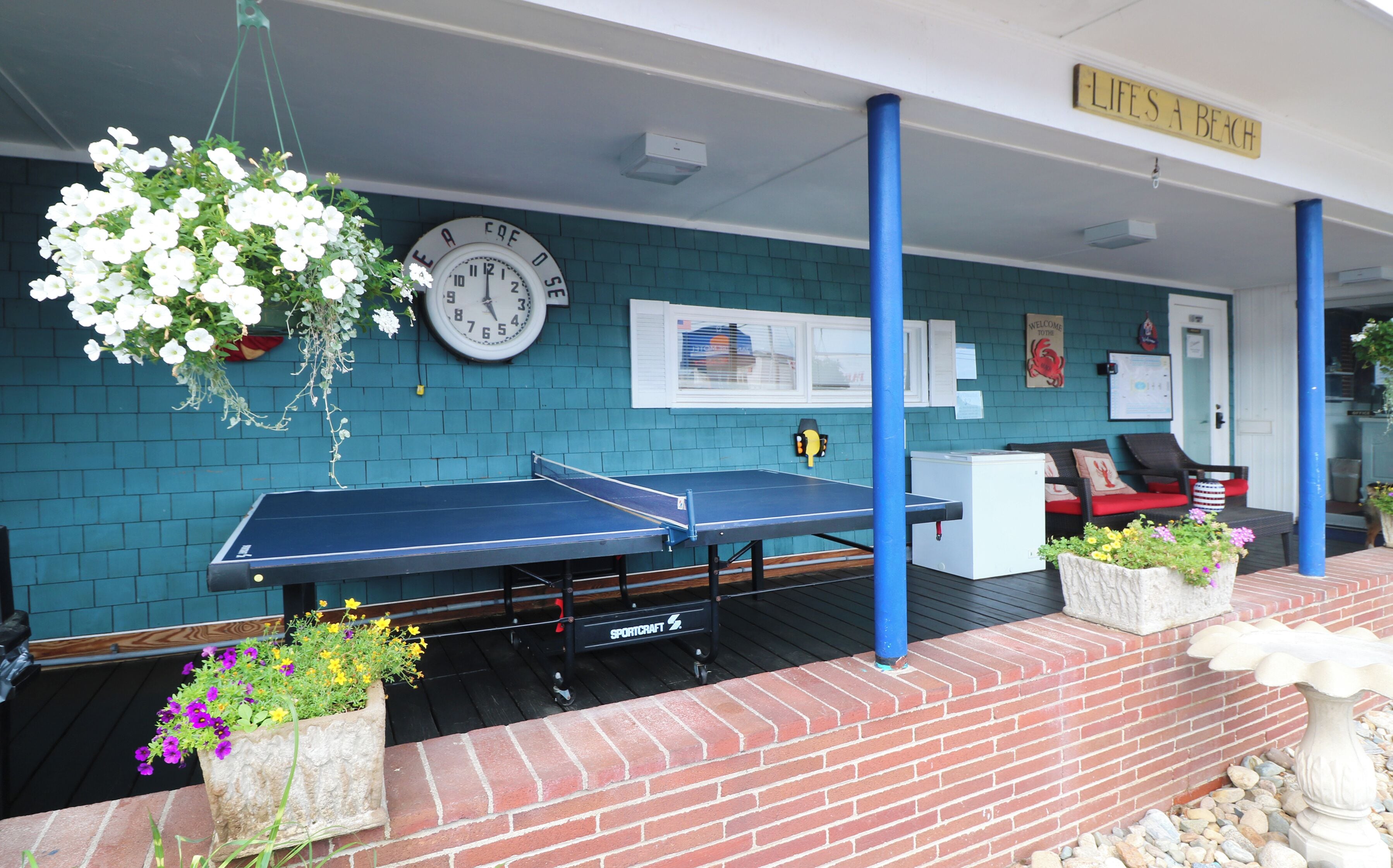 A covered outdoor area with a ping pong table, a clock, and a sign reading "LIFE'S A BEACH".