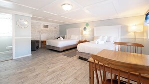 Habitación de hotel con dos camas, una mesa de comedor de madera, una silla, una mesita con lámpara y una ventana con cortinas.