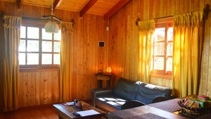A wooden cabin interior with a sofa, a table, and a window with curtains.