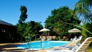 A swimming pool with lounge chairs and umbrellas, surrounded by lush greenery and a clear blue sky.