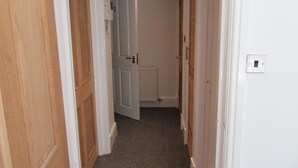 Un couloir étroit, avec des portes en bois de chaque côté, un radiateur blanc et un interrupteur sur le mur.