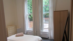 Une chambre à coucher avec un lit, une commode, un radiateur et une fenêtre avec des rideaux.
