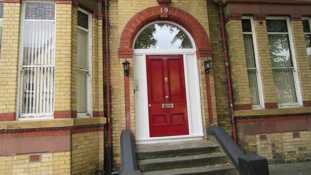 A red door with the number 19 above it, flanked by two windows with white frames and a small window with a barred design. - No 3 at Ivanhoe (Liverpool)