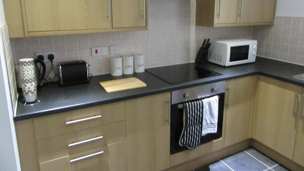A kitchen with wooden cabinets, a black countertop, a toaster, a microwave, and a stove.