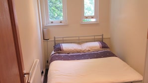 A small, narrow room with a single bed, a radiator, and two windows with curtains. - No 7 (Liverpool)