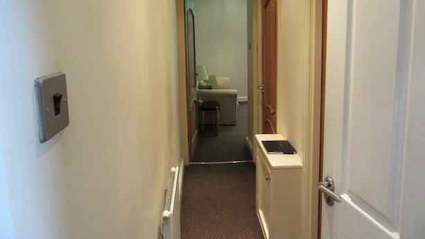 A narrow hallway with a radiator, a light switch, and a door leading to a room with a bed and a nightstand. - No 7 (Liverpool)