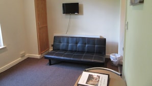 A small room with a black sofa, a television mounted on the wall, a wooden wardrobe, and a small table with a book. - No 7 (Liverpool)