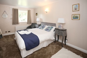 A neatly arranged bedroom with a bed, bedside lamps, a clock, and a window with curtains. - Merrymouth Inn (Chipping Norton)