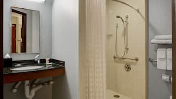 Un baño con lavamanos, espejo, ducha y toallero.