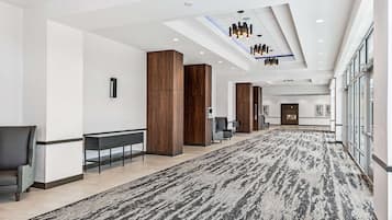 A spacious hallway with a patterned carpet, wooden columns, and modern lighting fixtures.