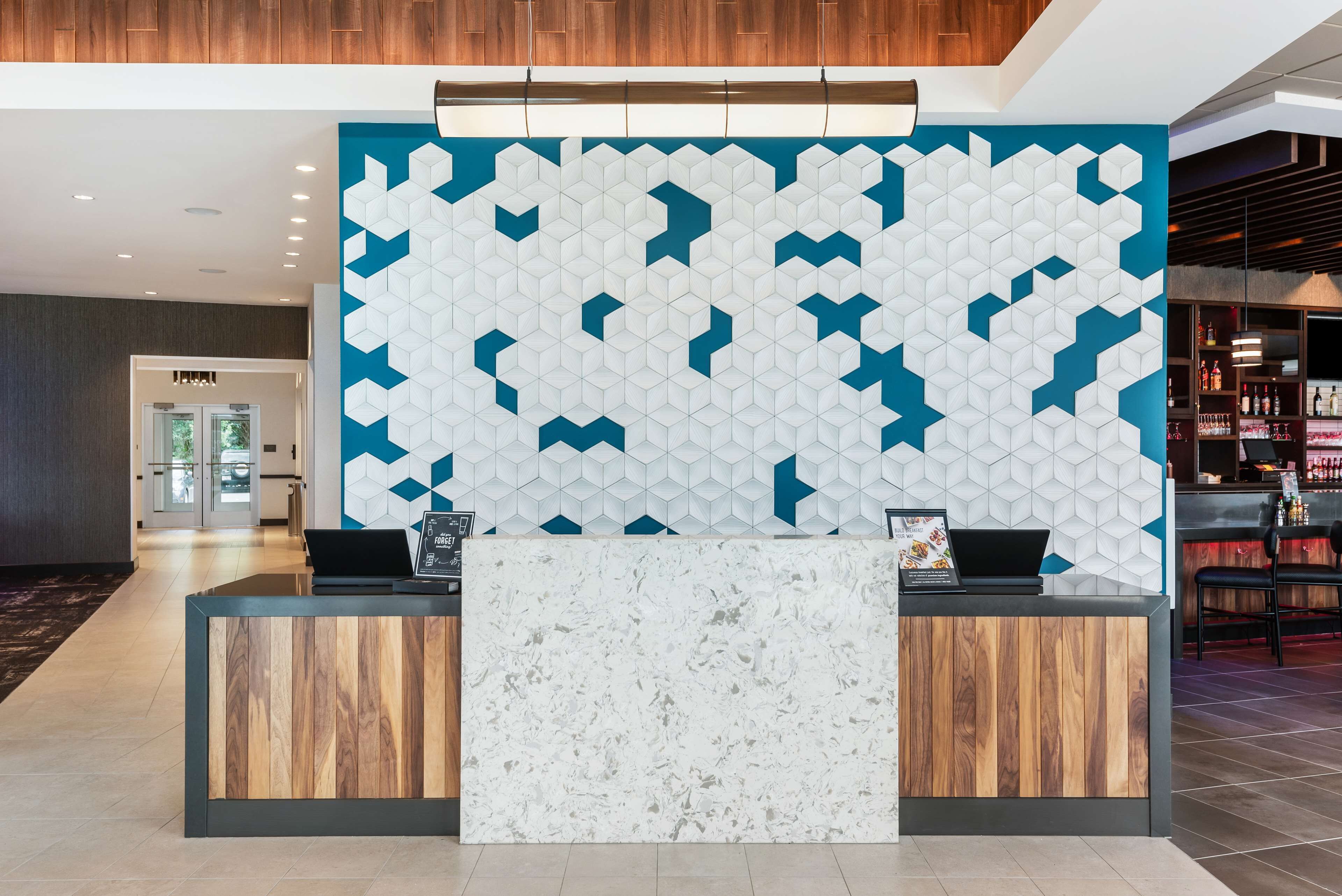 A reception desk with a geometric patterned wall, a wooden reception area, and a bar area in the background.