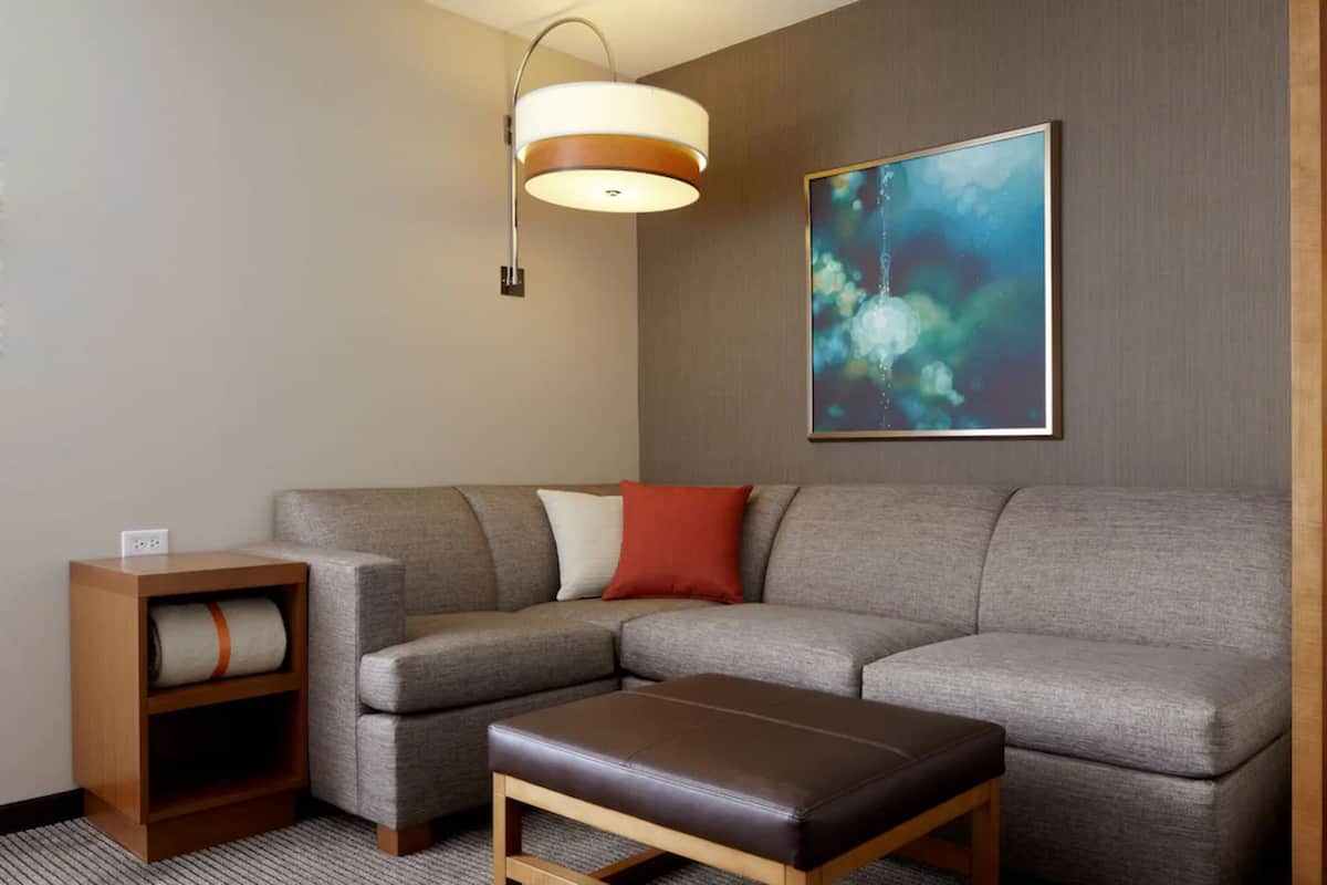 A modern living room with a sectional sofa, a wooden bench, a side table with a lamp, and a framed abstract painting on the wall.