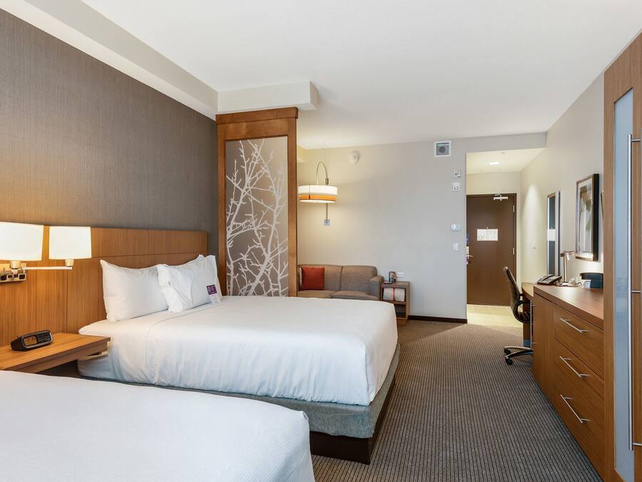 Een hotelkamer met twee bedden, een bureau met stoel, een dressoir en een zichtbare badkamer door een geopende deur.