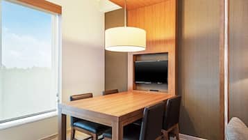 Un comedor moderno con una mesa de madera, seis sillas, un televisor montado en la pared y un ventanal que ofrece vistas al exterior.