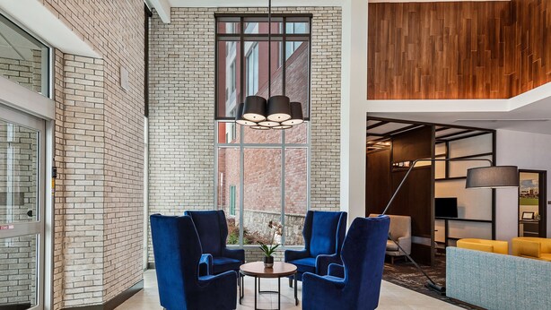 Een moderne lobby met bakstenen muren, een groot raam en blauwe stoelen rond een bijzettafeltje.