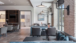 Un hall d’hôtel moderne doté d’un espace repas, de différents coins salon et d’une grande fenêtre laissant entrer la lumière naturelle.
