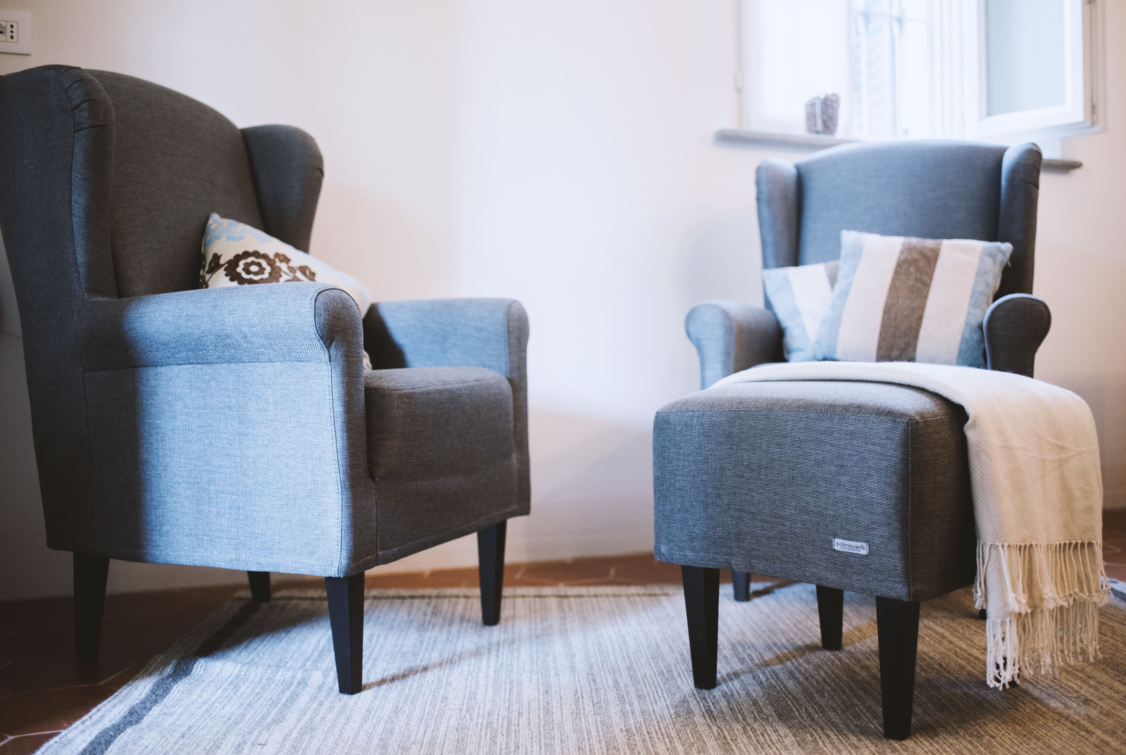 Two armchairs with different patterns, a rug, and a window with curtains.