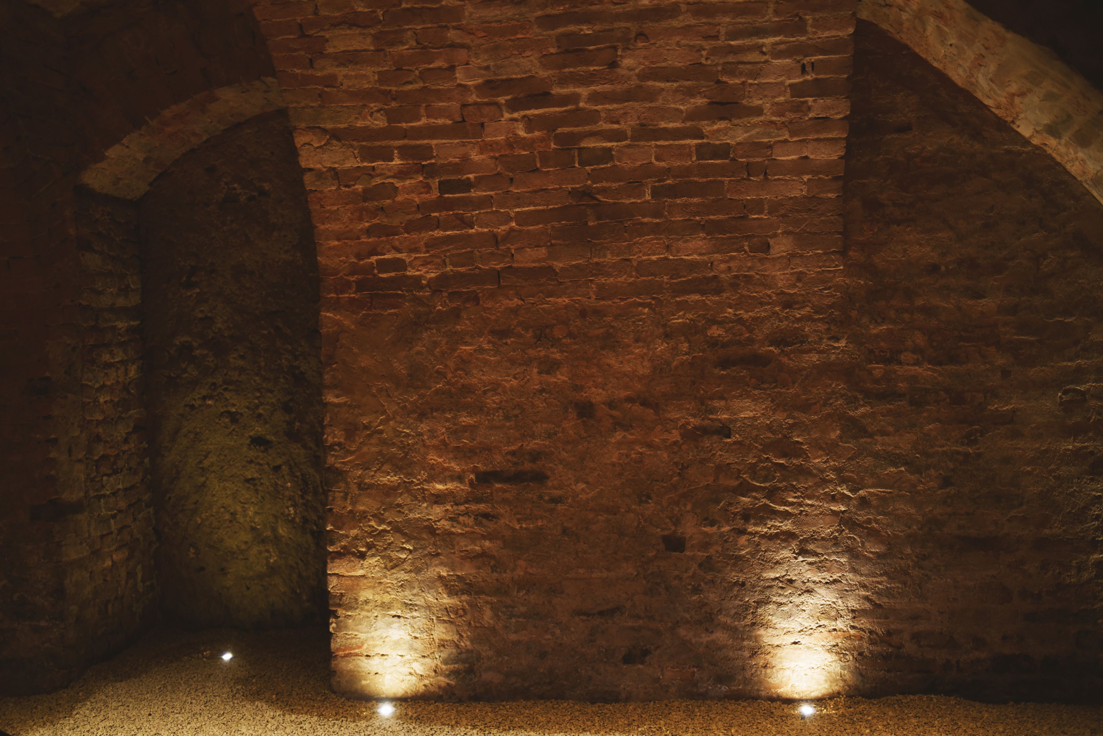 A dimly lit brick wall with a single light source at the base, creating a spotlight effect.