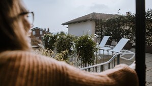 A person sitting on a chair overlooking a patio area with a white building and a garden. - Moonfrà (Antignano)