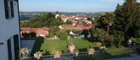 Zona residencial con vistas a un pueblo, un edificio blanco con contraventanas verdes y un césped cuidado con plantas en macetas.