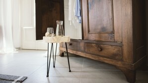 A wooden cabinet with drawers, a small table with a glass pitcher, and a glass on the floor. - Moonfrà (Antignano)