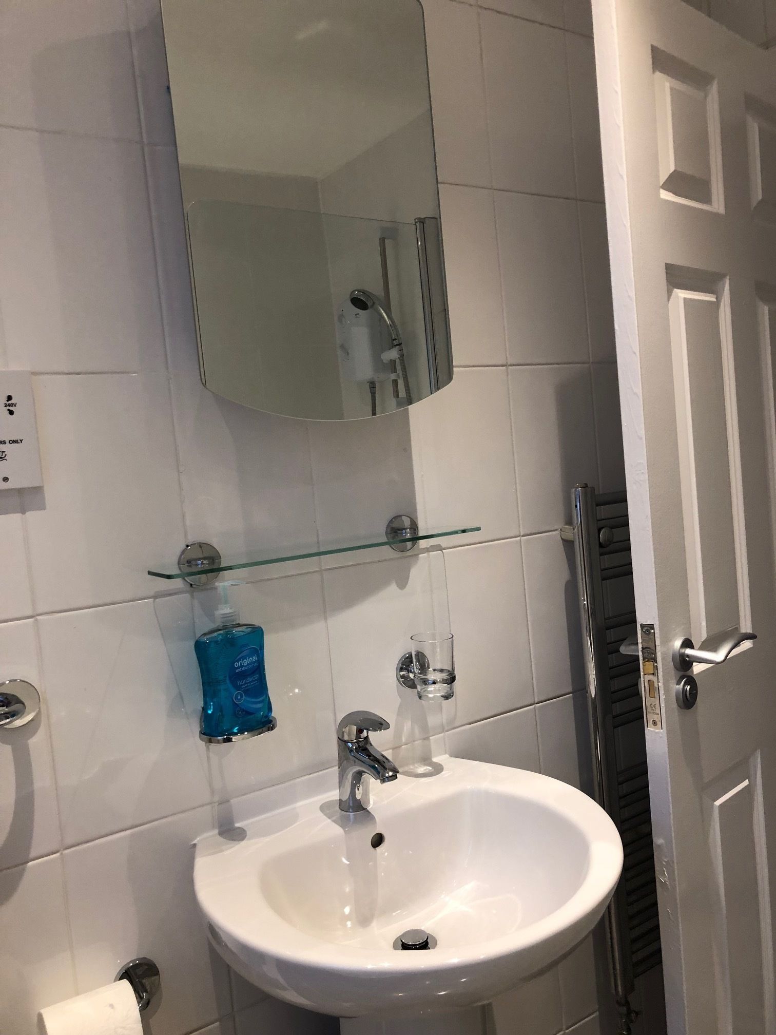 A bathroom with a white sink, a glass shelf with a blue bottle, a mirror above the sink, and a door to the right.