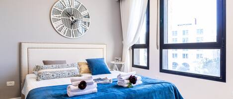 A modern bedroom with a large bed, a decorative clock, and a view of a building through a window.