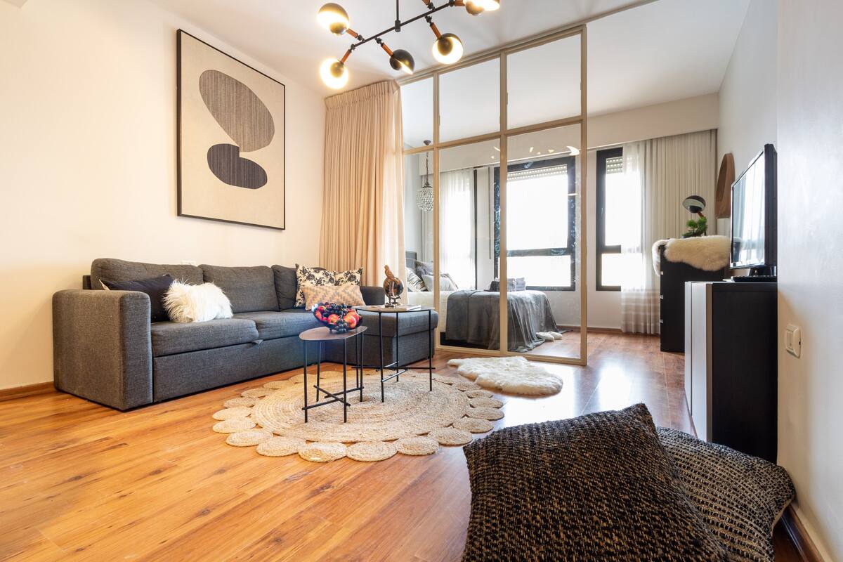 Ein modernes Wohnzimmer mit einem grauen Sofa, einem Couchtisch und einem großen Fenster mit Vorhängen.