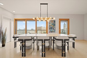 Un comedor moderno con una mesa grande y seis sillas, ventanas amplias con vista a la ciudad y una lámpara colgante.