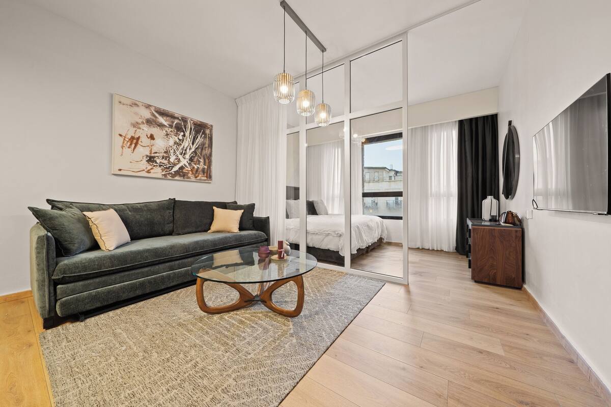 Ein modernes Wohnzimmer mit einer Couch, einem Glastisch und einem großen Fenster mit Vorhängen.