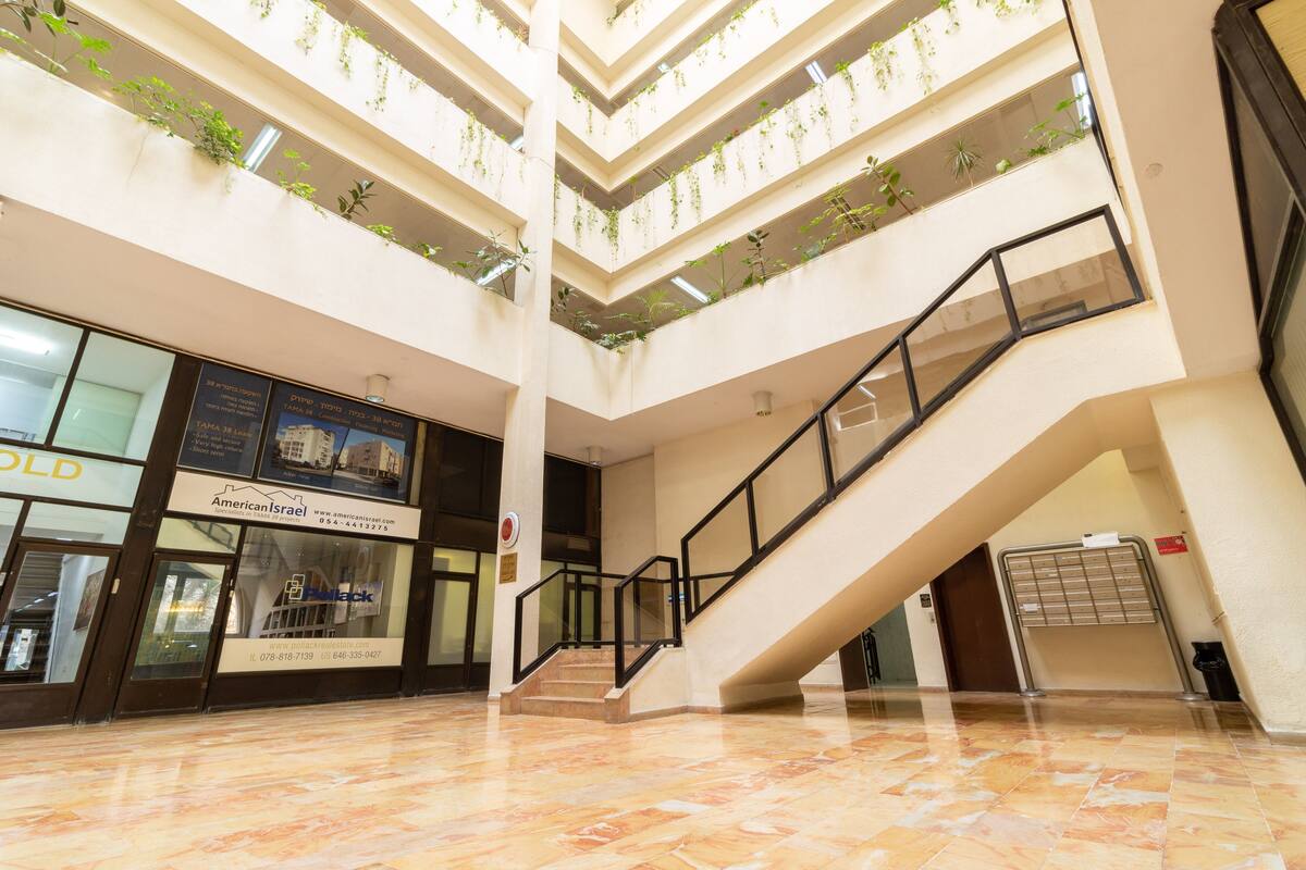 Ein mehrgeschossiges Atrium mit Treppe, Glasgeländern und Bepflanzung auf Balkonen.