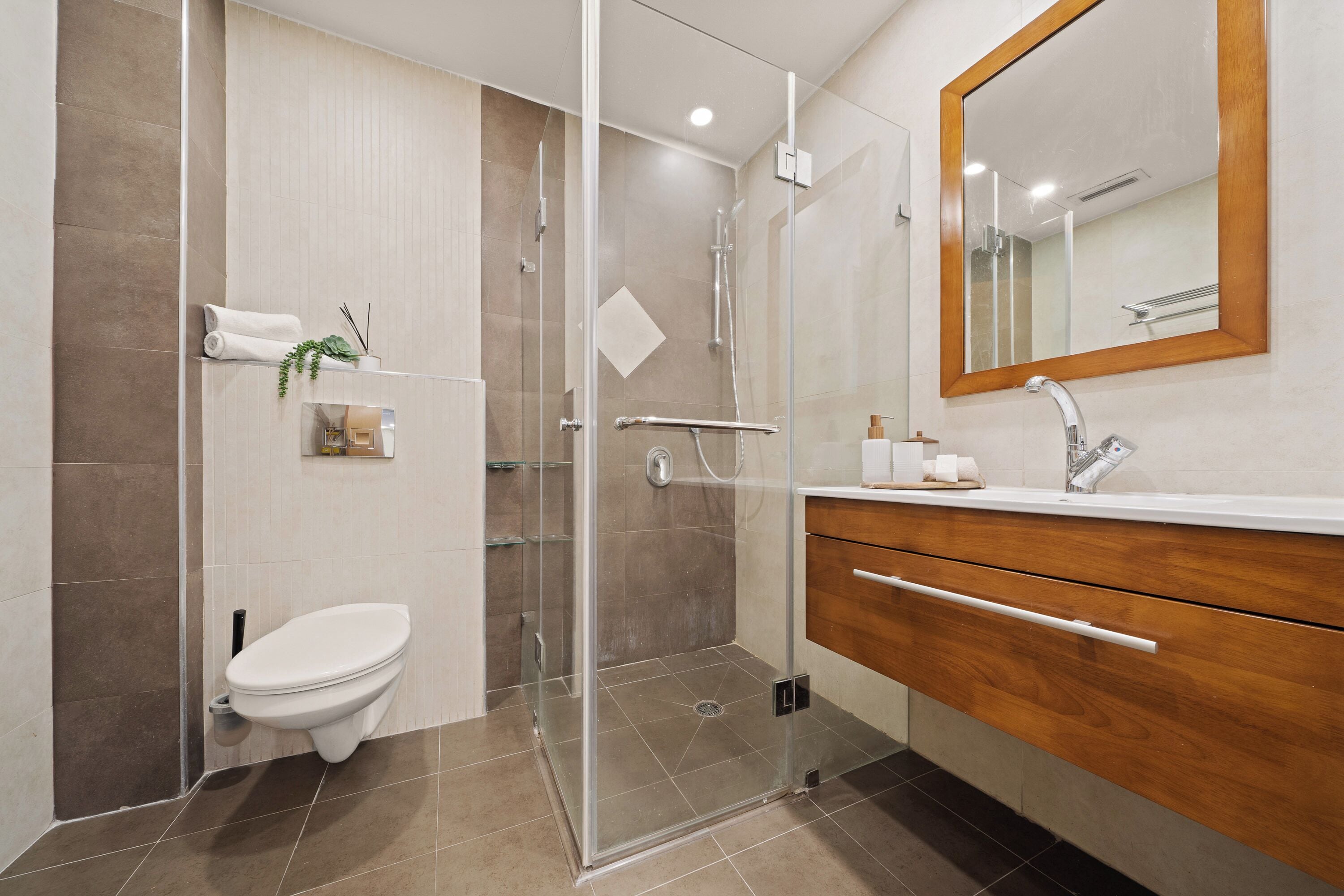 A modern bathroom with a glass-enclosed shower, a white toilet, and a wooden vanity with a mirror.