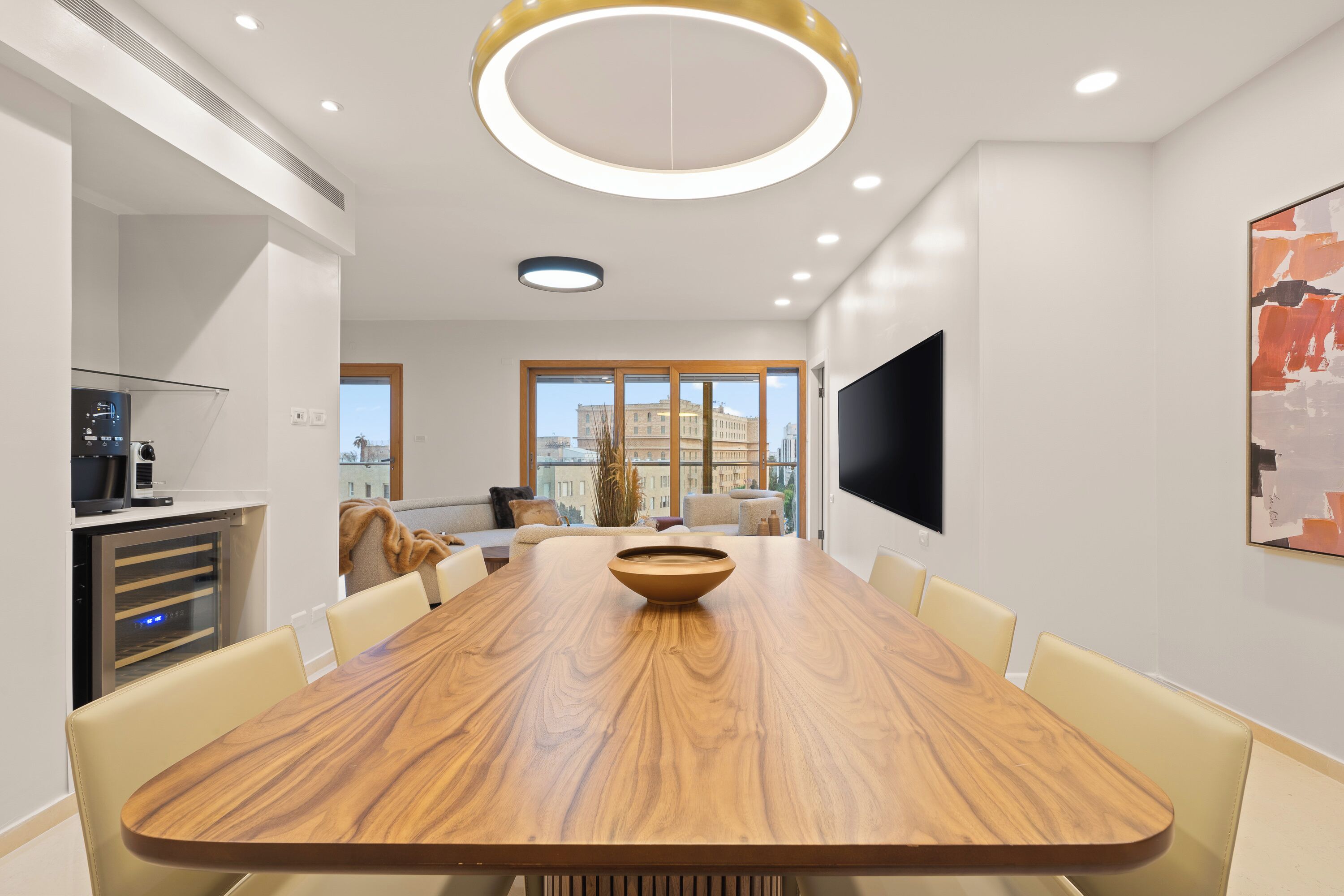 Un espace repas moderne avec une table en bois, des sièges confortables, une grande fenêtre donnant sur la ville et un téléviseur à écran plat fixé au mur.