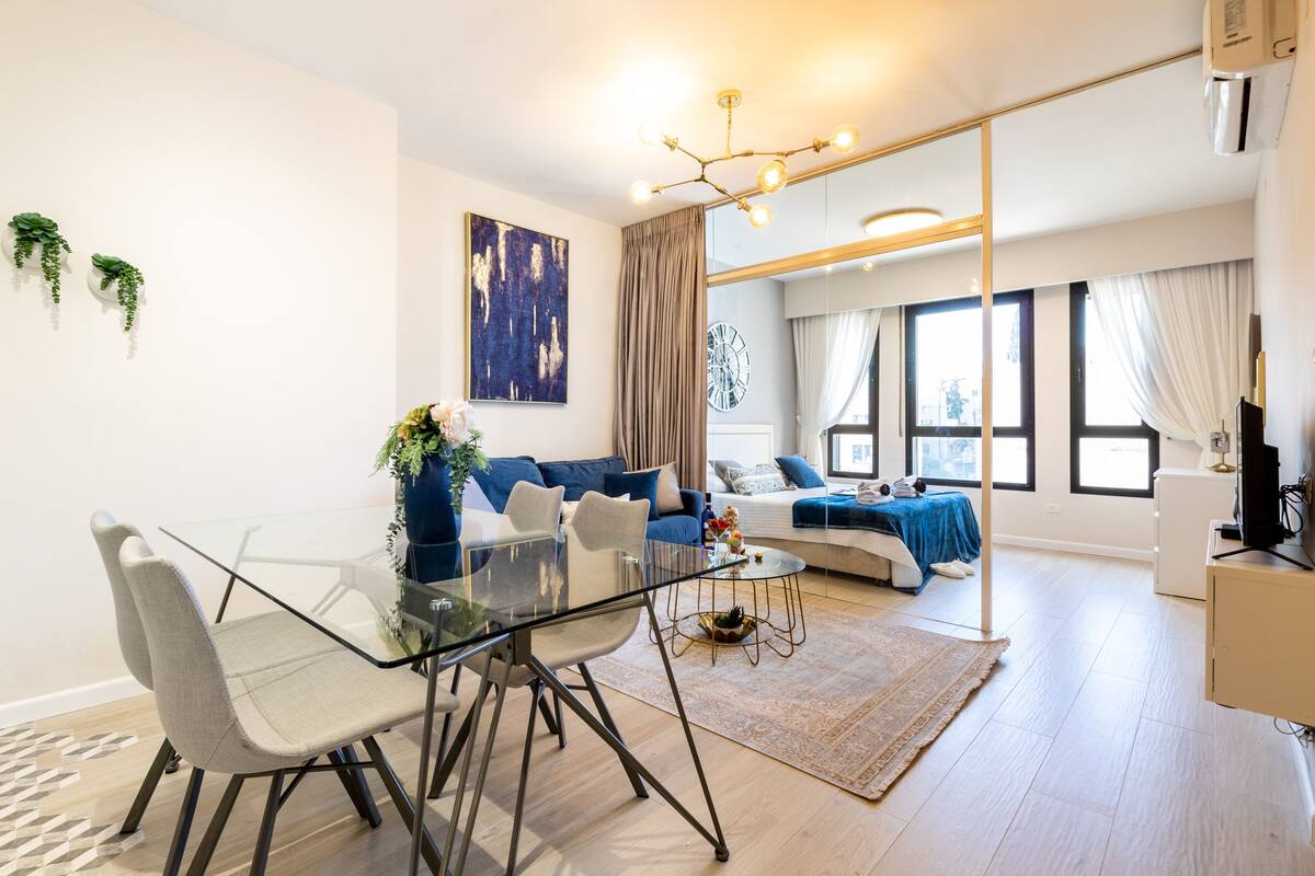 Ein modernes Wohnzimmer mit einem Glastisch, einer Sofagarnitur und einem großen Fenster mit Vorhängen.