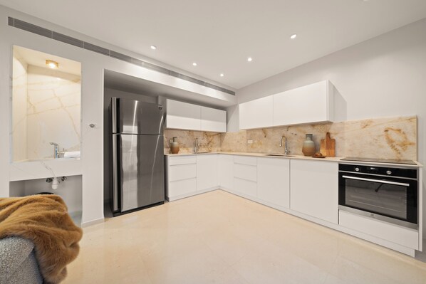 A modern kitchen with white cabinets, a stainless steel refrigerator, an oven, and marble countertops.
