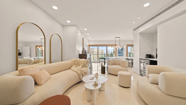 A modern living room with a large sectional sofa, a coffee table, and a kitchen area in the background. - King David Court - Isrentals (Jerusalem)