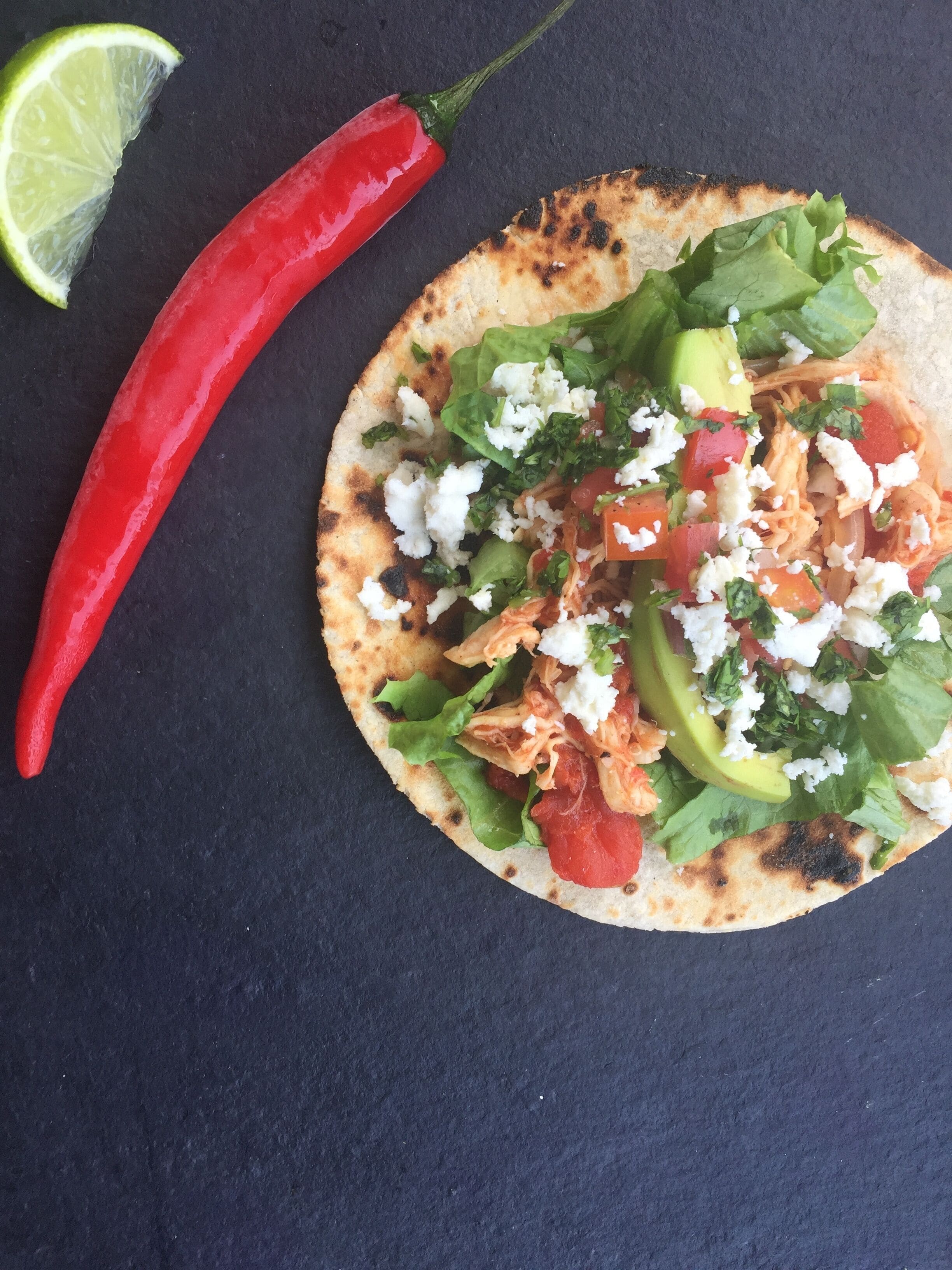 Un taco con lechuga, tomates, aguacate y queso sobre pan plano.