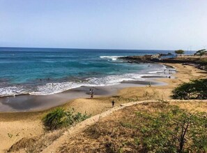 A beach with clear blue water, sandy shore, and some vegetation. - Syds Guesthouse I (Praia)