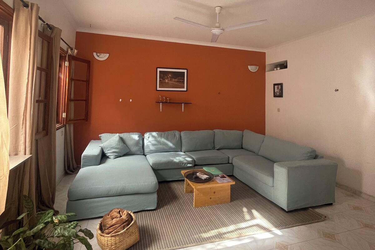 A living room with a light blue sectional sofa, a wooden coffee table, and a ceiling fan.