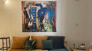 A living room with a sofa, coffee table, and a painting on the wall. - Syds Guesthouse I (Praia)