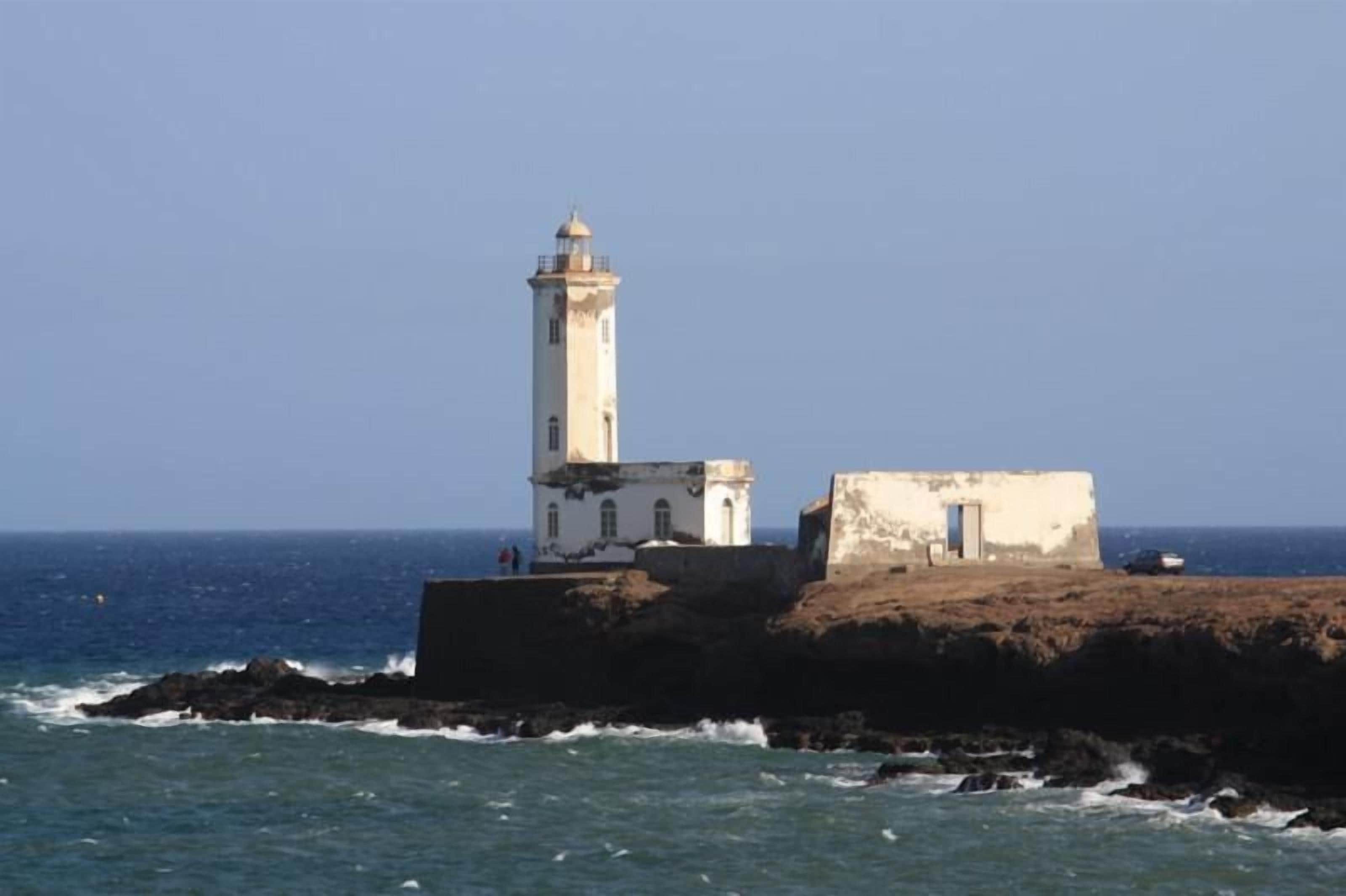 Un faro su uno sperone roccioso con un piccolo edificio adiacente, affacciato sul mare.
