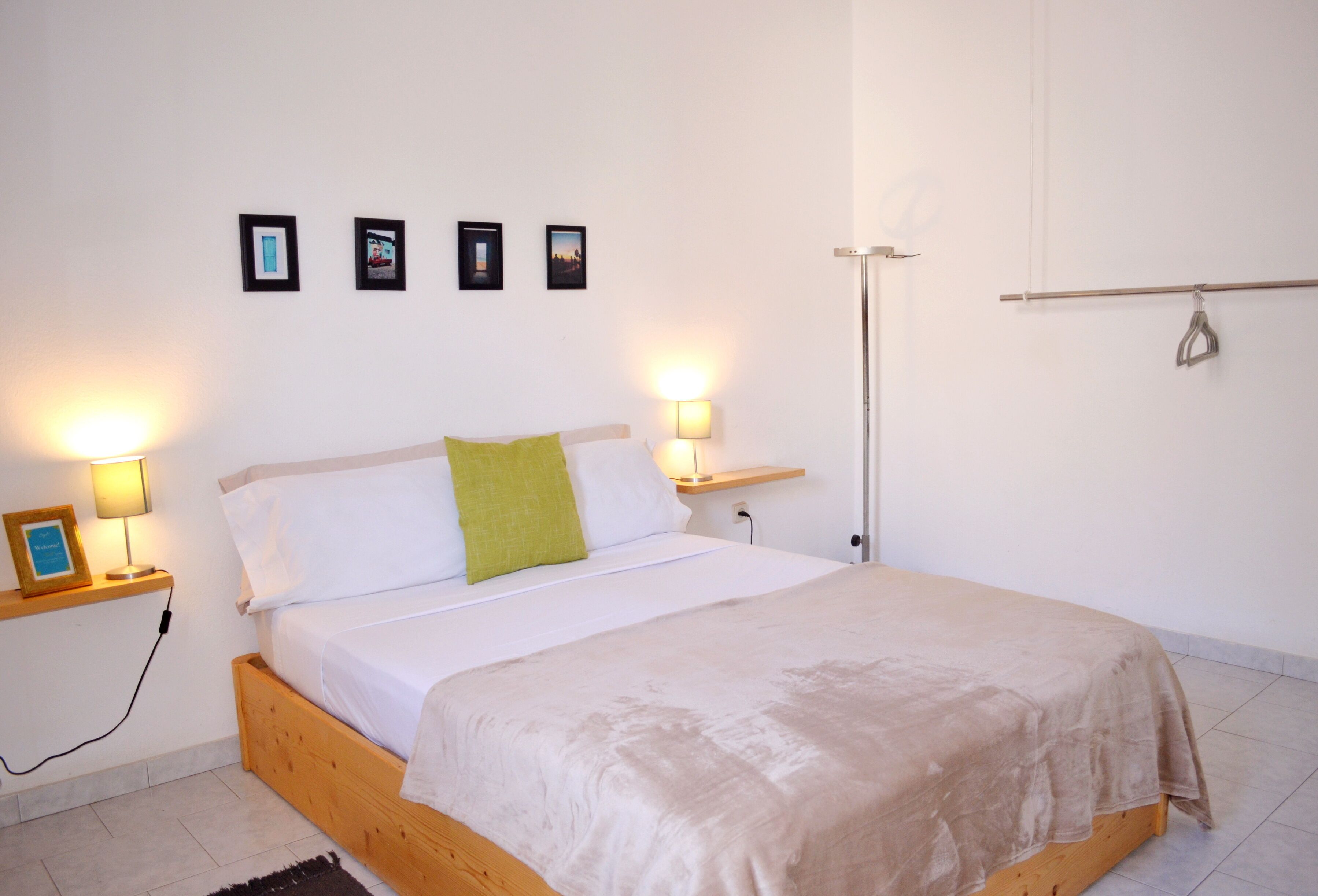Un dormitorio con una cama de madera, ropa de cama blanca, un almohadón verde, lámparas de noche y cuadros en la pared.