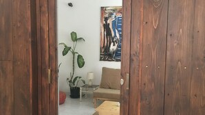 A wooden door leading into a room with a sofa, a lamp, a potted plant, and a painting on the wall. - Syds Guesthouse I (Praia)