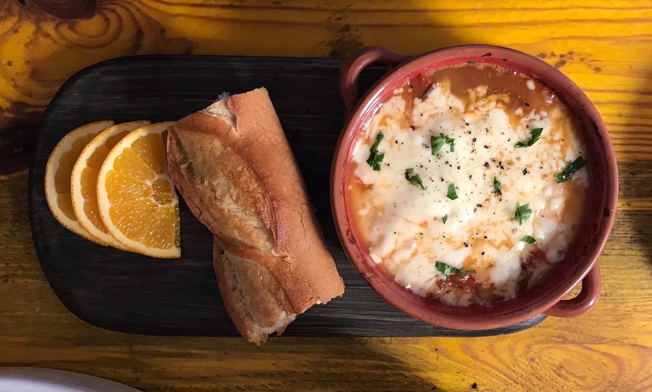 A bowl of soup with bread and orange slices on a wooden board.