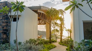 A modern building with a stone facade, a covered outdoor seating area, and a pathway lined with tropical plants. - 2 Bedroom Apartment, Private Pool - Luna 03 (SAn Juan del Sur)