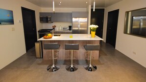 A modern kitchen with a central island, bar stools, stainless steel appliances, and pendant lighting. - 2 Bedroom Apartment, Private Pool - Luna 03 (SAn Juan del Sur)