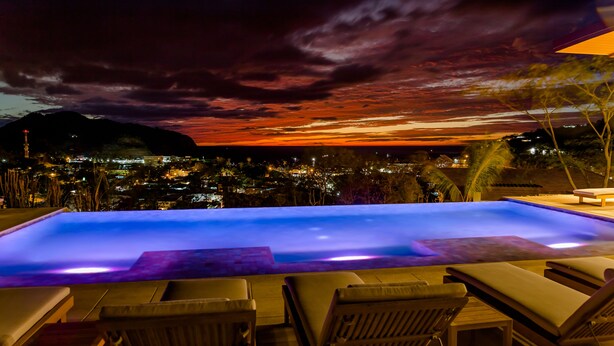 A swimming pool with lounge chairs, a view of a cityscape at sunset, and a mountain in the background. - 2 Bedroom Apartment, Private Pool - Luna 03 (SAn Juan del Sur)