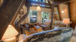 Un intérieur de chalet chaleureux avec un canapé, des fauteuils, un téléviseur et une table à manger.