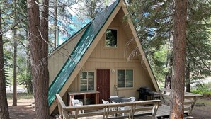 Une cabane avec un toit triangulaire, une terrasse en bois et un petit espace porche avec des chaises.
