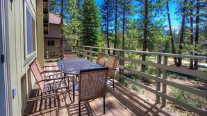 Eine Holzdar Terrasse mit Tisch und Stühlen, umgeben von einem Holzgeländer, mit Blick auf einen bewaldeten Bereich.